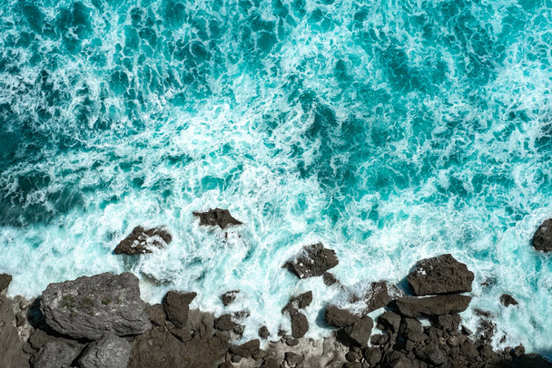 Öfkeli mavi okyanus dalgaları suda köpükle kayaların üzerinde kırılır. - Fotoğraf, Görsel