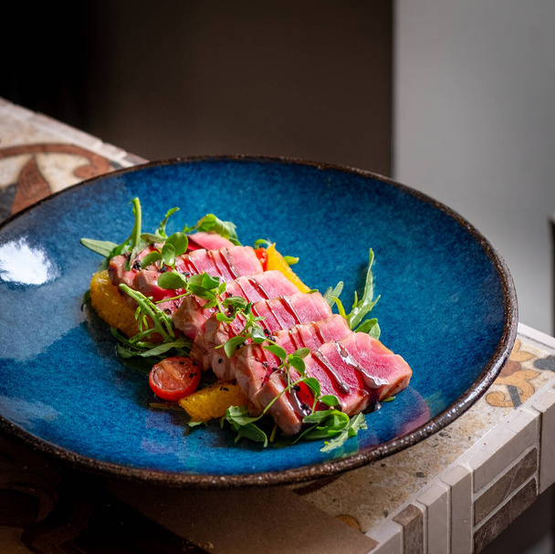 Krájený grilovaný tuňák se zeleným salátem a rajčaty na talíři na dřevěném pozadí. - Fotografie, Obrázek
