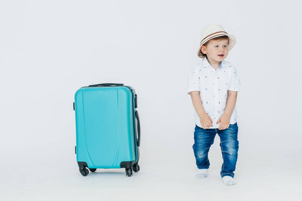 A boy with glasses and a hat is going to go on vacation, looks slyly from under his glasses. Leaning on a blue suitcase. The child is happy, smiling and laughing. Summer, vacation. - Valokuva, kuva