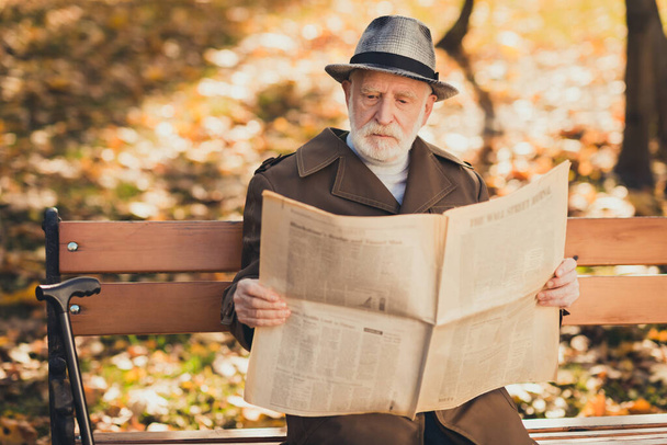 Photo of focused old man grandfather sit bench autumn town park read interesting bought newspaper wear cap headwear - Zdjęcie, obraz