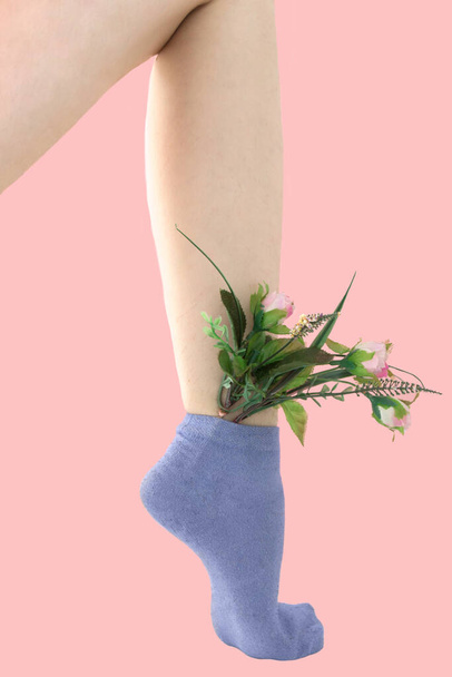A nő borotválatlan lába kék zokniban. Rózsaszín virágok vannak a zokniban. rózsaszín háttér. - Fotó, kép