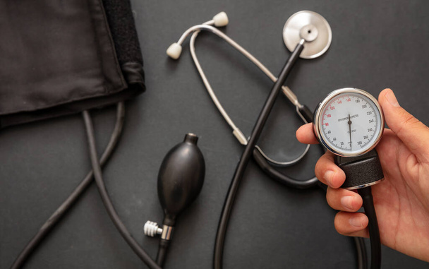 Blutdruckmessung, Hand hält Blutdruckmessgerät auf schwarzem Hintergrund, Nahaufnahme. - Foto, Bild