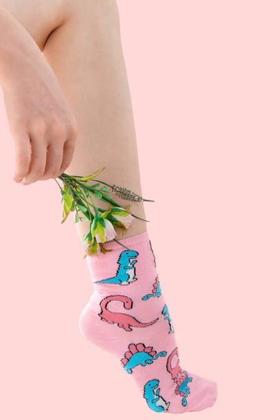 Woman's unshaven leg in pink socks with dinosaurs on a pink background. - Photo, Image