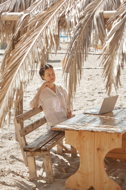 Mujer joven usando un ordenador portátil en una playa. Concepto de trabajo independiente - Foto, Imagen