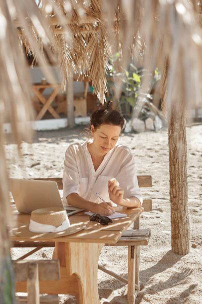 Mujer joven usando un ordenador portátil en una playa. Concepto de trabajo independiente - Foto, imagen