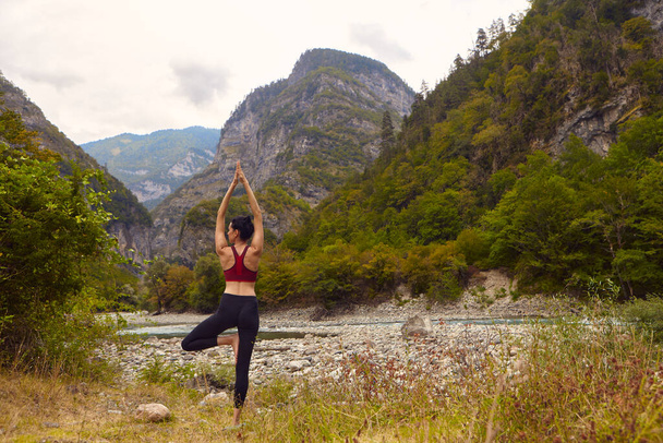 Aulas de ioga na natureza. Uma mulher faz ioga nas montanhas, perto de um rio de montanha flui. O conceito de praticar esportes sozinho. Exclusão social - Foto, Imagem