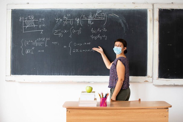 Female teacher with mask teaching math lesson at school. Social distanting and classroom safety during coronavirus epidemic - Фото, изображение