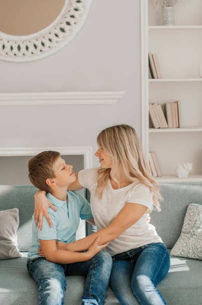 Mom and kid are laughing together in cozy home. They are holding each other with joy while relaxing on sofa. Parent is playfully touching boy feet and he is enjoying i - Foto, Imagen