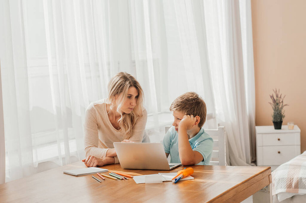 Mom helping little boy to do homework. Mother and son drawing together, mom helping with homework. Cute boy doing his school homework with his mother, at home, he is writing on a book - Photo, image