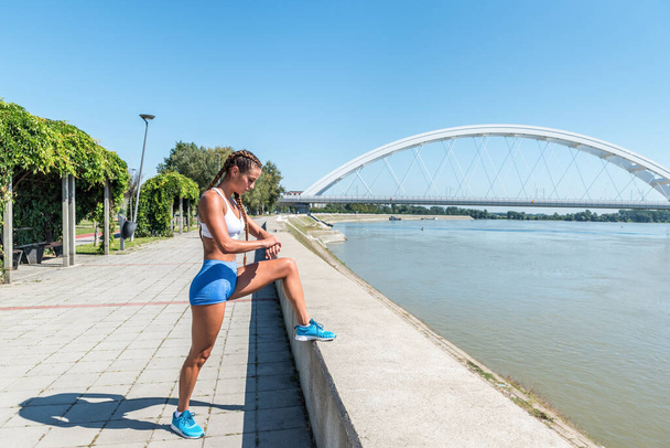 Young sexy muscular fit woman in shorts taking a break and look at her risk watch after hard outdoor cross workout training - Foto, Imagem