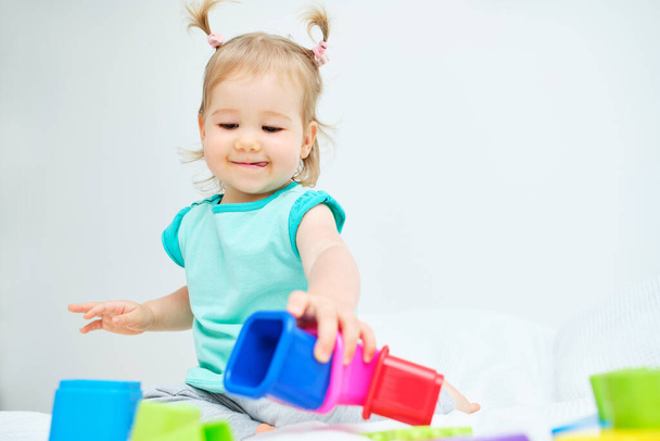 Καυκάσιος νήπιο παίζει με πολύχρωμα παιχνίδια στο κρεβάτι. - Φωτογραφία, εικόνα