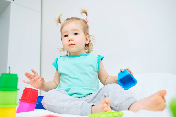 Caucasian toddler sitting on the bed among toys. - Photo, Image