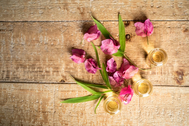 Essential oil in small glass bottles with bamboo leaves, bougainvillea and frangipani flowers on wooden background. Selective focus. top view and copy space for text. Natural cosmetics. - Photo, Image