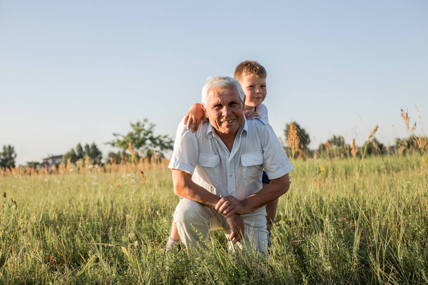 Onnellinen lapsi isoisän kanssa leikkimässä niityllä. Isoisä jää eläkkeelle. Eläkevanhempi - Valokuva, kuva