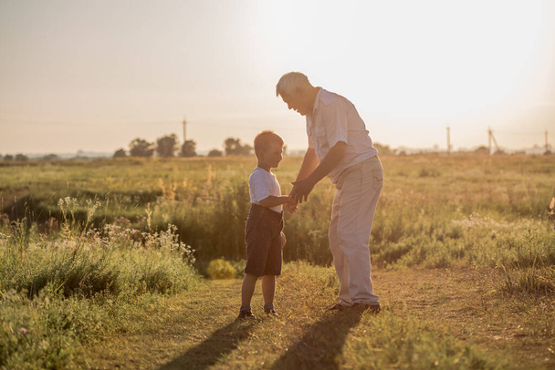 Happy senior man Grandfather with cute little boy grandson playing in field. - Photo, Image