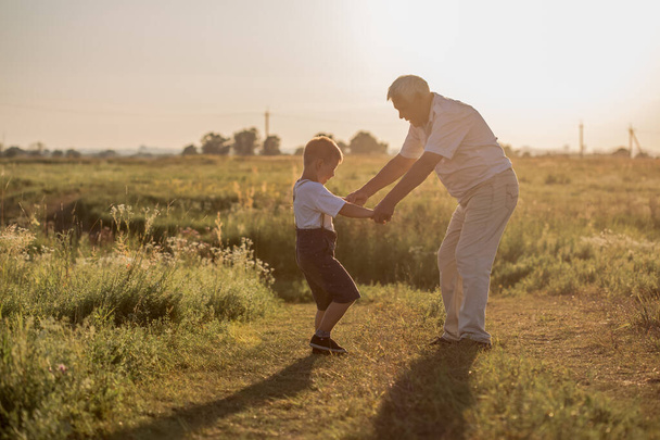Счастливый старший дедушка с милым маленьким внуком, играющим в поле.. - Фото, изображение