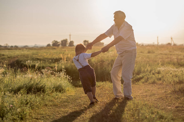 Happy senior man Grandfather with cute little boy grandson playing in field. - Фото, изображение