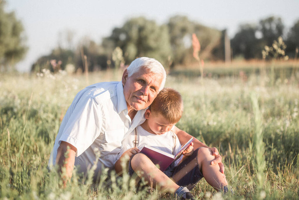 Средний снимок дедушки и его внука во время чтения книги вместе на лугу Маленький мальчик делает первые шаги в чтении. - Фото, изображение