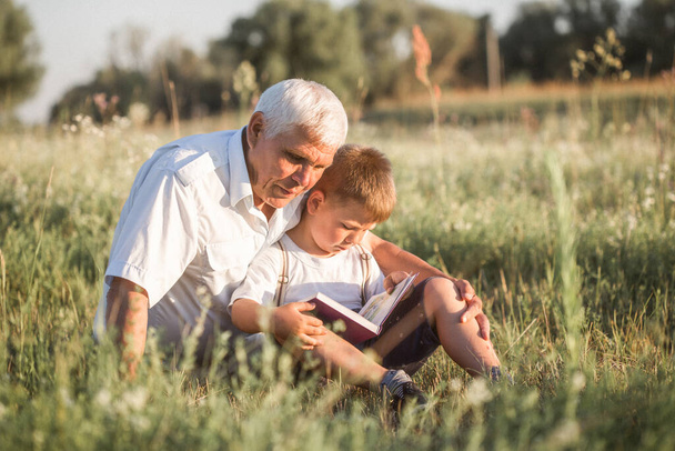 Välillä laukaus isoisän ja hänen pojanpoikansa lukiessaan kirjaa yhdessä niitty Pieni poika tekee ensimmäiset askeleet lukea. - Valokuva, kuva
