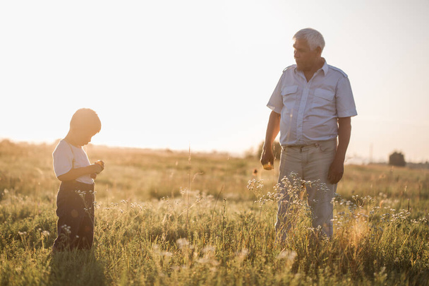 Boldog öregember nagyapa aranyos kisfiú unokájával játszik a mezőn. Boldog gyermek nagyapa játszik a szabadban - Fotó, kép