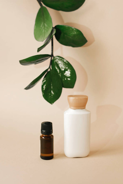 A plastic bottle with body care cream and a glass bottle with oil on a beige background, as well as a leaf of a tropical plant. Organic natural cosmetics - Photo, Image