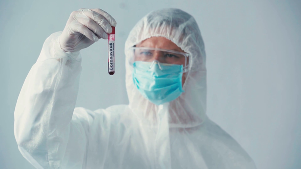cientista em tubo de teste de retenção de terno hazmat com amostra de sangue isolada em cinza - Filmagem, Vídeo