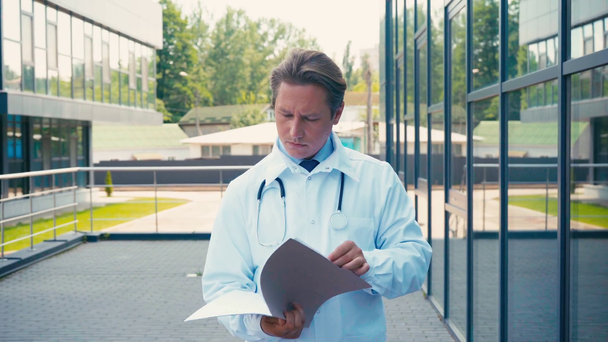 orvos fehér köpeny gazdaság mappa és séta mellett klinika kívül - Felvétel, videó