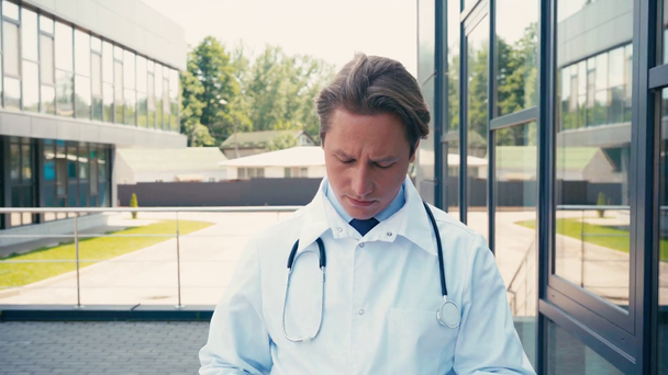 medico in camice bianco togliersi la maschera medica e camminare vicino alla clinica all'esterno - Filmati, video