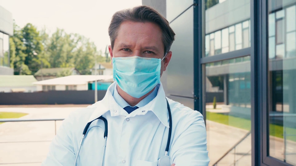 arts in medisch masker staan in de buurt van kliniek en kijken naar camera  - Video