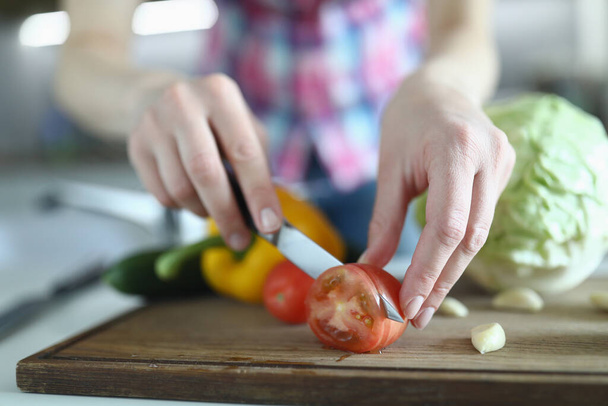 Η γυναίκα φτιάχνει σαλάτα και κρατάει μαχαίρι στο χέρι της και κόβει την ντομάτα σε φέτα. - Φωτογραφία, εικόνα