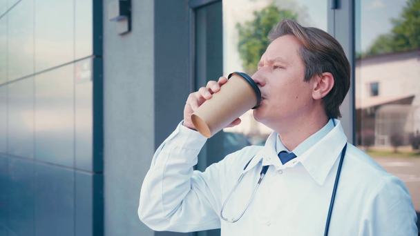 γιατρός σε λευκό παλτό πίνοντας καφέ για να πάει κοντά στην κλινική  - Πλάνα, βίντεο