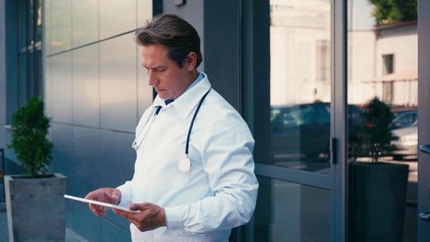 orvos fehér kabátban, digitális tablettát használva a klinikán kívül  - Felvétel, videó