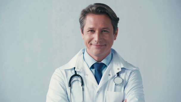 doctor in white coat with stethoscope looking at camera on grey - Video