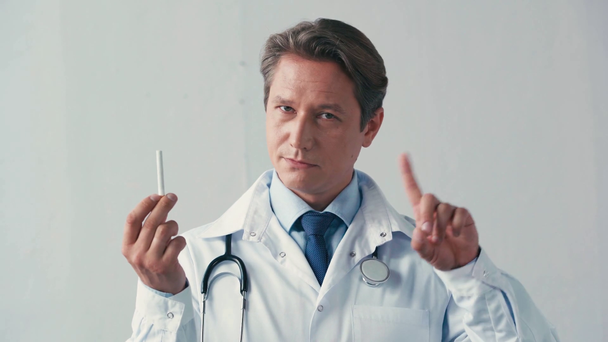 lääkäri valkoisessa takissa pitelee savuketta eikä osoita elettä harmaalla - Materiaali, video