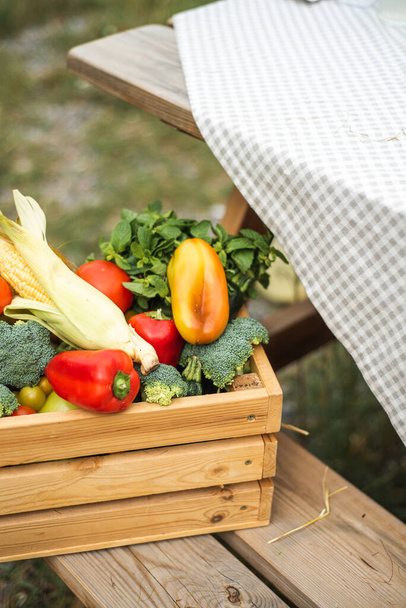 A box with a harvest of vegetables is on the street. Peppers, corn, broccoli, tomatoes and herbs inside the box. Autumn harvest. - Fotoğraf, Görsel