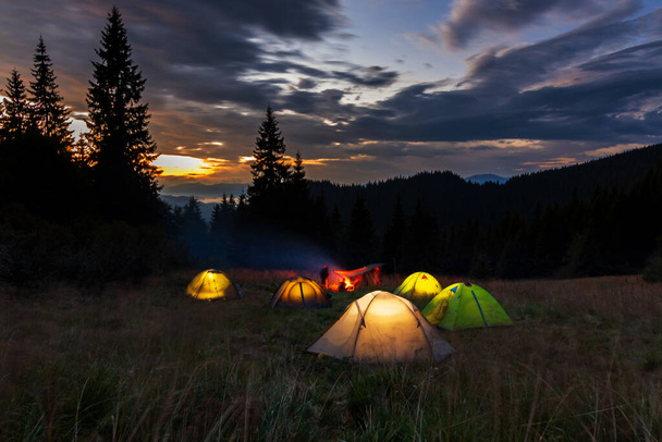 Avond in de Oekraïense Karpaten. Tenten gloeien op het gazon op een achtergrond van zonsondergang. Kamperen in de bergen. - Foto, afbeelding