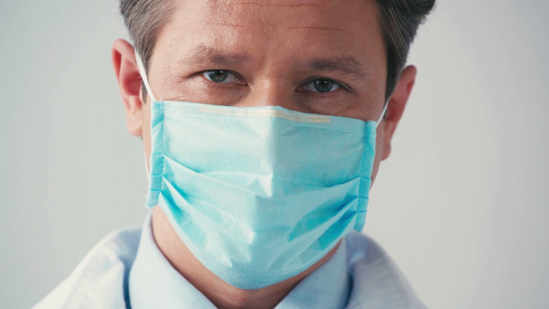 close up de médico em máscara médica olhando para a câmera em cinza - Filmagem, Vídeo