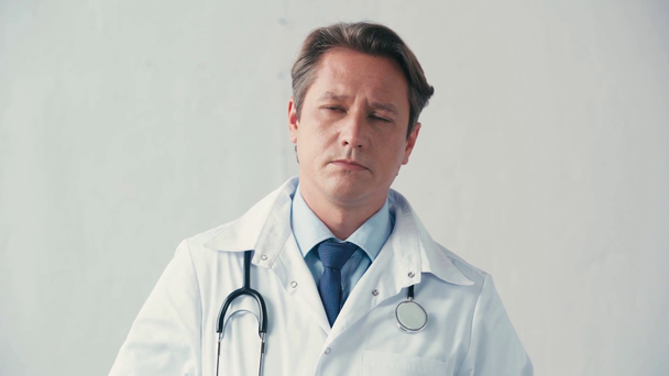 lääkäri valkoisessa takissa riisuu lääketieteellisen maskin harmaalla  - Materiaali, video