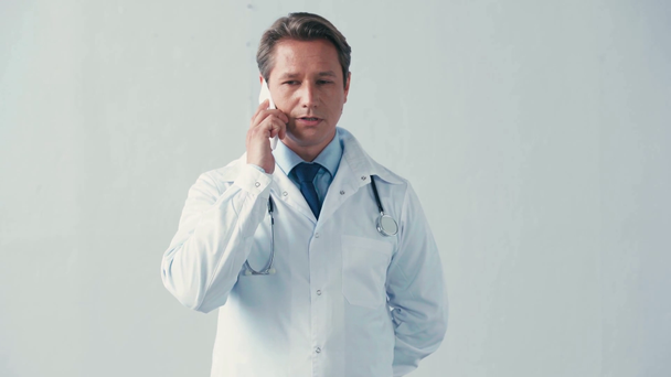доктор в белом халате разговаривает по смартфону на сером  - Кадры, видео