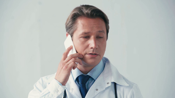 serious doctor in white coat talking on smartphone on grey  - Footage, Video