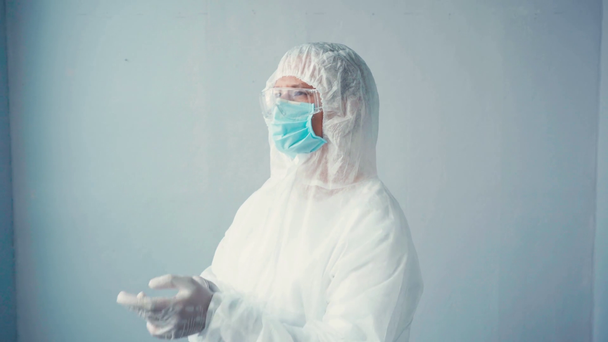 scientist in hazmat suit and medical mask wearing latex gloves on grey - Footage, Video