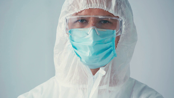 vědec v hazmat obleku a lékařské masky při pohledu na kameru izolované na šedé - Záběry, video
