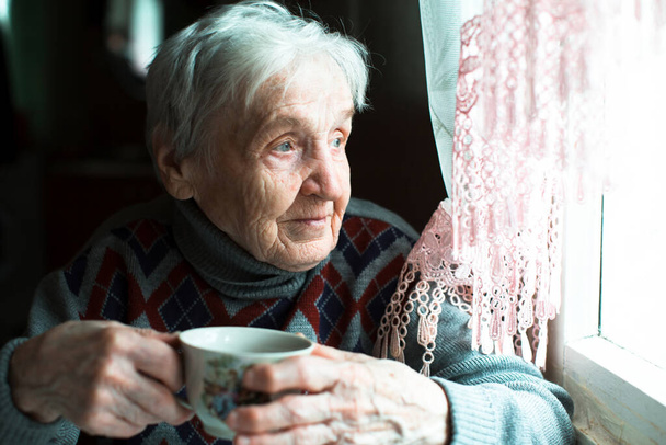 Μια γριά γυναίκα πίνει τσάι καθισμένη στην κουζίνα.. - Φωτογραφία, εικόνα