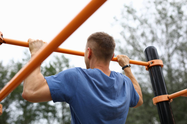 Man in blue t-shirt pull himself up on horizontal bar in park. - Foto, immagini