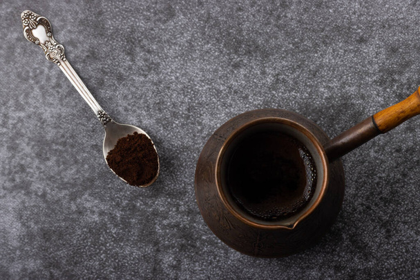 Top view of vintage cezve with brewed coffee and a spoon with ground coffee on grey background - Photo, Image