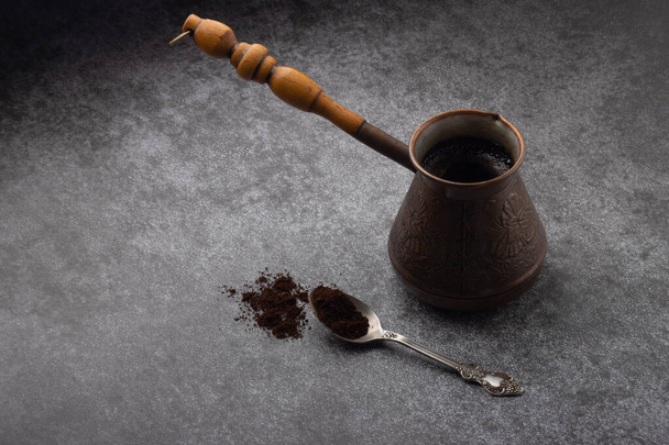Vintage cezve with brewed coffee and a spoon with ground coffee on grey background. Coffee concept - Fotografie, Obrázek