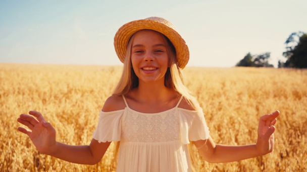 ragazza in abito bianco toccare cappello di paglia e ridere nel campo di grano  - Filmati, video