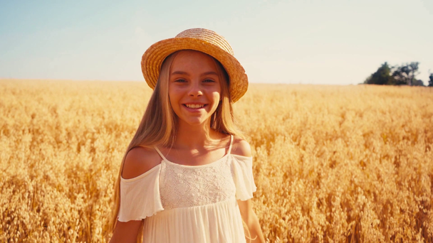 κορίτσι σε λευκό φόρεμα στροφή γύρω και αγγίζοντας ψάθινο καπέλο στον τομέα του σιταριού  - Πλάνα, βίντεο