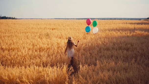 zpět pohled na dívku v bílých šatech chůze s balónky v pšeničném poli - Záběry, video