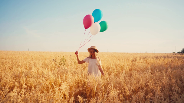 dítě v bílých šatech a slamák chůze s barevnými balónky v pšeničném poli - Záběry, video